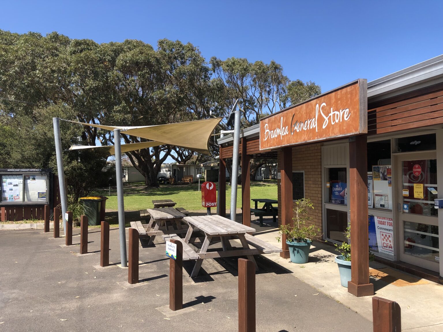 the outside of the Breamlea General store, including tables, wooden bollards, trees and grass and a blue sky